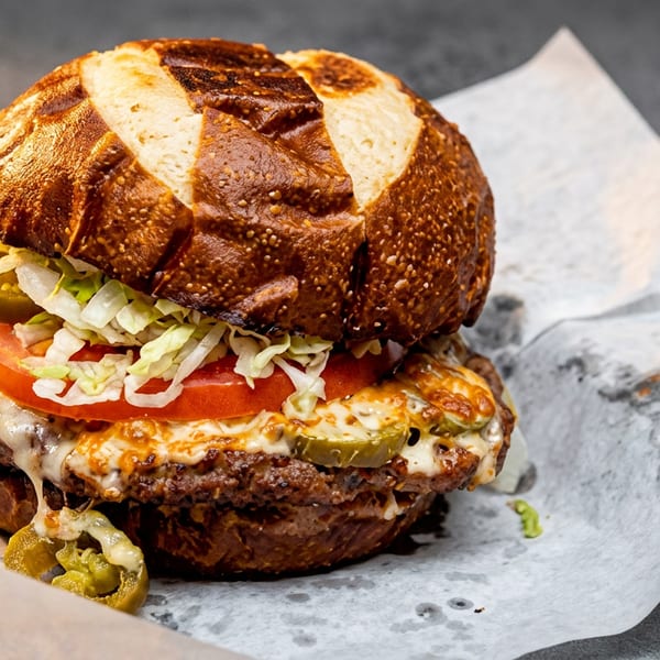 A juicy burger with melted cheese, tomatoes, lettuce, and jalapeños on a pretzel bun.