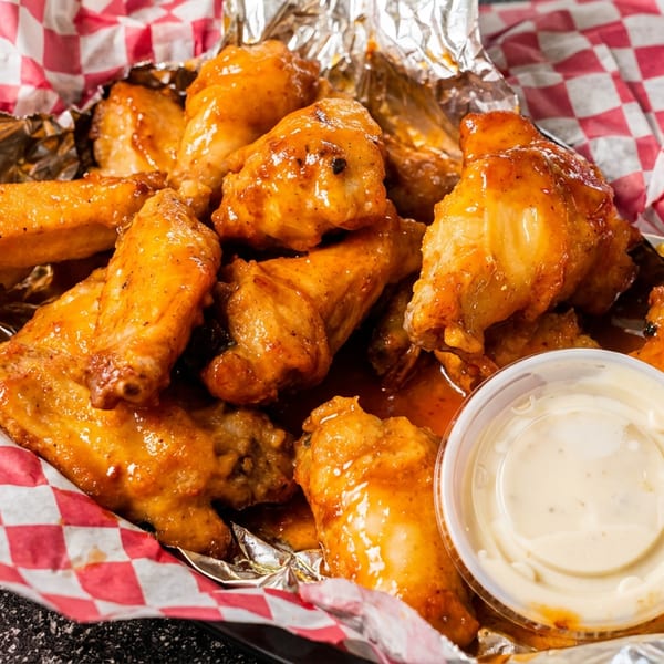A basket of golden-brown chicken wings coated in sauce, with a side of dipping sauce.