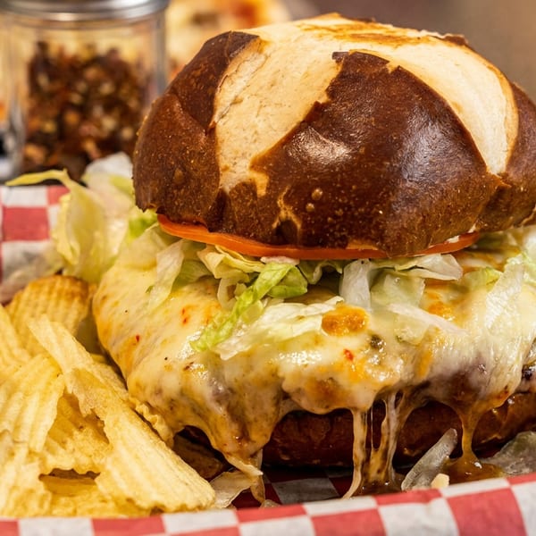 Cheesy burger on a pretzel bun with lettuce, tomato, and a side of ruffled potato chips.